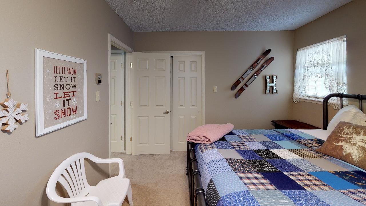 A bedroom with a bed, a chair, a door, and a wall with a framed sign.