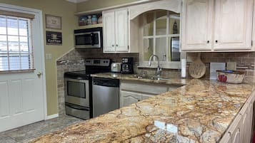 A kitchen with granite countertops, stainless steel appliances, and light wooden cabinets.
