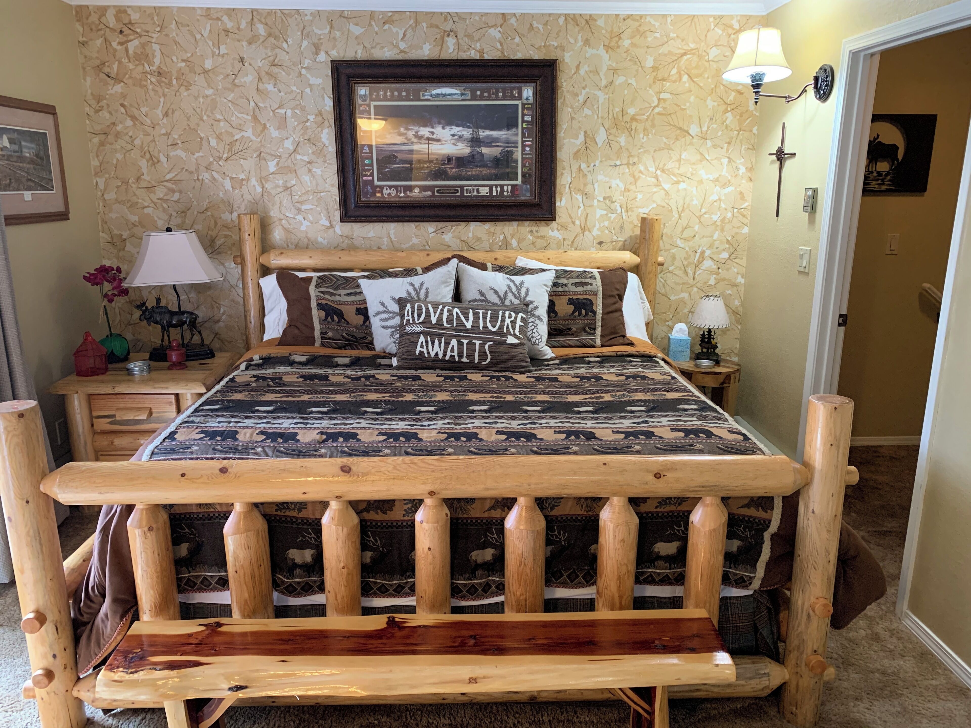 Un lit en bois, recouvert d’une couvre-lit à motifs et agrémenté d’un coussin sur lequel est brodé le mot « AVENTURE ».