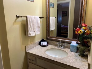 Un baño con lavamanos, espejo, toallero y un florero con flores.