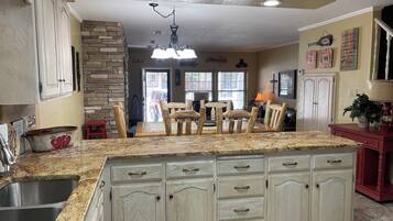 A kitchen with granite countertops, white cabinetry, a stone accent wall, and a dining area with wooden chairs.