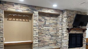 Ein Kamin aus Stein mit darüber montiertem Fernseher, Holzregalen und einer Sitzbank.
