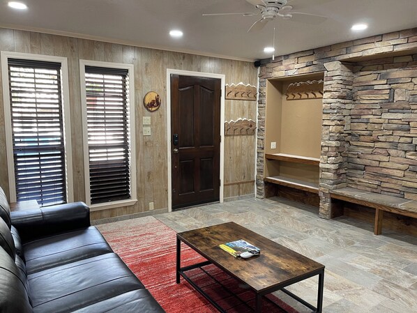 Una sala de estar con un sofá de cuero, una mesa de centro, una pared de acento de piedra y una puerta con panel de madera.