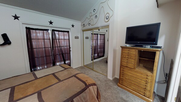 A hotel room with a bed, a television on a wooden cabinet, and a mirror reflecting the room.