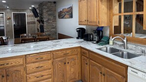 Eine Küche mit Holzausstattung, einer Wand aus Naturstein, einem Essbereich mit Tisch und Stühlen sowie einer Kaffeemaschine.