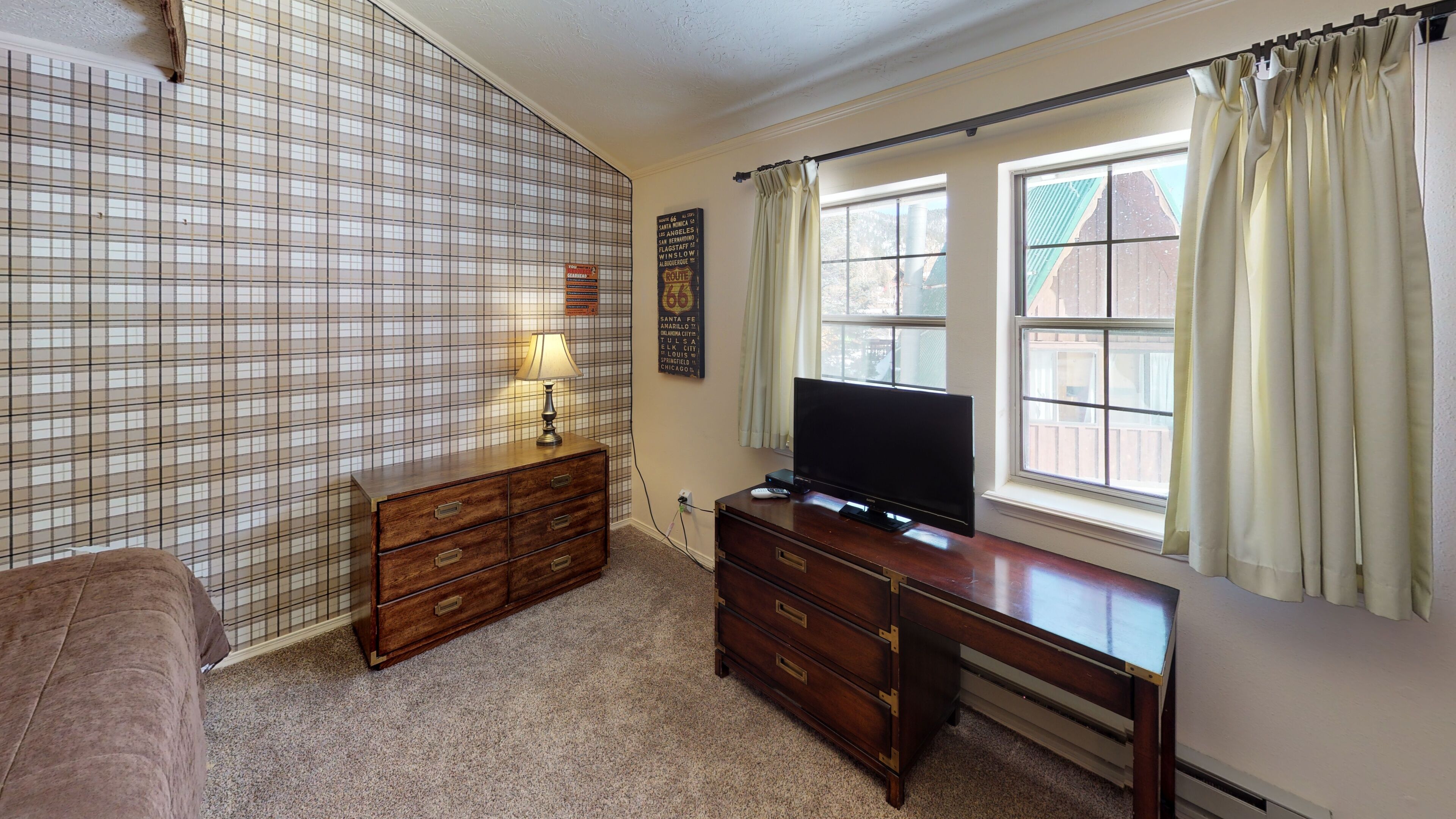 A bedroom with a large window, a television, a dresser, and a lamp.