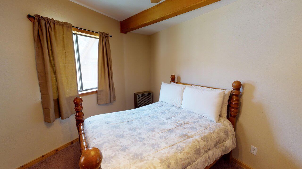A bedroom with a wooden bed frame, a window with curtains, and a radiator.