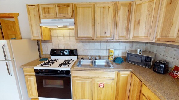 A kitchen with wooden cabinets, a gas stove, a microwave, a toaster, and a sink.