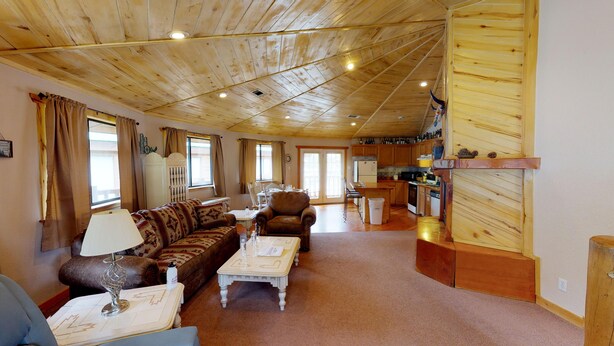 A spacious living area with a wooden ceiling, a sofa, a coffee table, and a dining table. A kitchen is visible in the background. - Round Eagle Home near the River and Park (Red River)