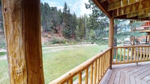 A wooden deck with a railing overlooking a grassy area and a forested hillside. - Round Eagle Home near the River and Park (Red River)