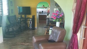 Uma sala de estar com um sofá de couro marrom, uma televisão e uma área de refeições ao fundo.