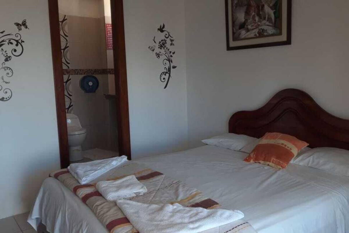 Un lit bien fait, avec une couverture à rayures et une serviette pliée, une tête de lit en bois et un tableau encadré accroché au mur.