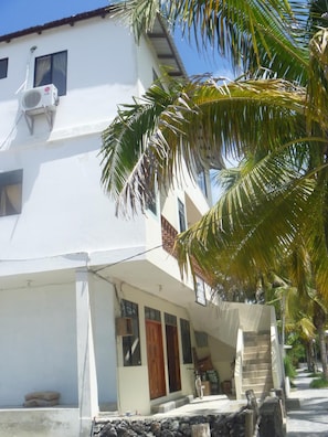 A two-story building with a white exterior, a wooden door, and a staircase leading to the entrance. - Hostal los Delfines (Puerto Villamil)