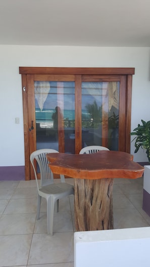 A wooden table with chairs in a room with a large glass door leading to a view of the ocean. - Hostal los Delfines (Puerto Villamil)