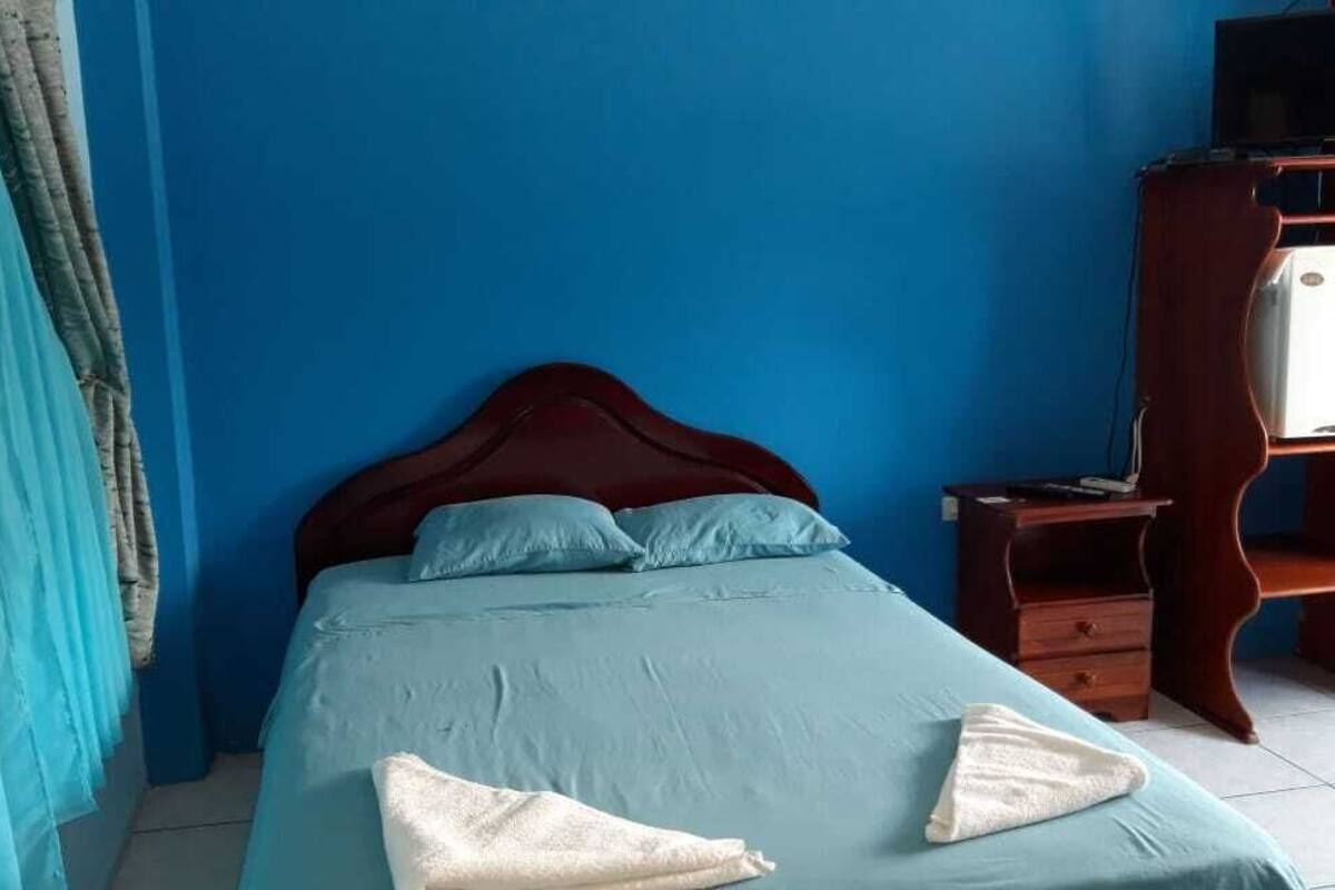 Une pièce avec un lit, une table de chevet en bois, une commode et un mur bleu.
