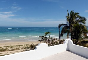 Une vue sur la plage, avec un balcon blanc, des palmiers et l’océan.