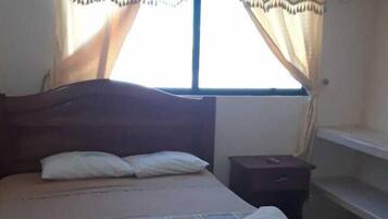 A bed with a patterned bedspread, a nightstand, and curtains on a window.