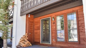 A wooden cabin with a front door, two windows, and a porch with a stack of firewood. - Claim Jumper #17 Townhouse (Red River)