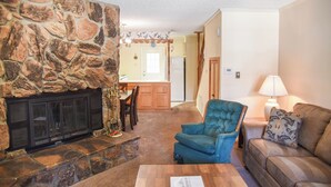 A living room with a stone fireplace, a blue armchair, a sofa, and a lamp. - Claim Jumper #17 Townhouse (Red River)