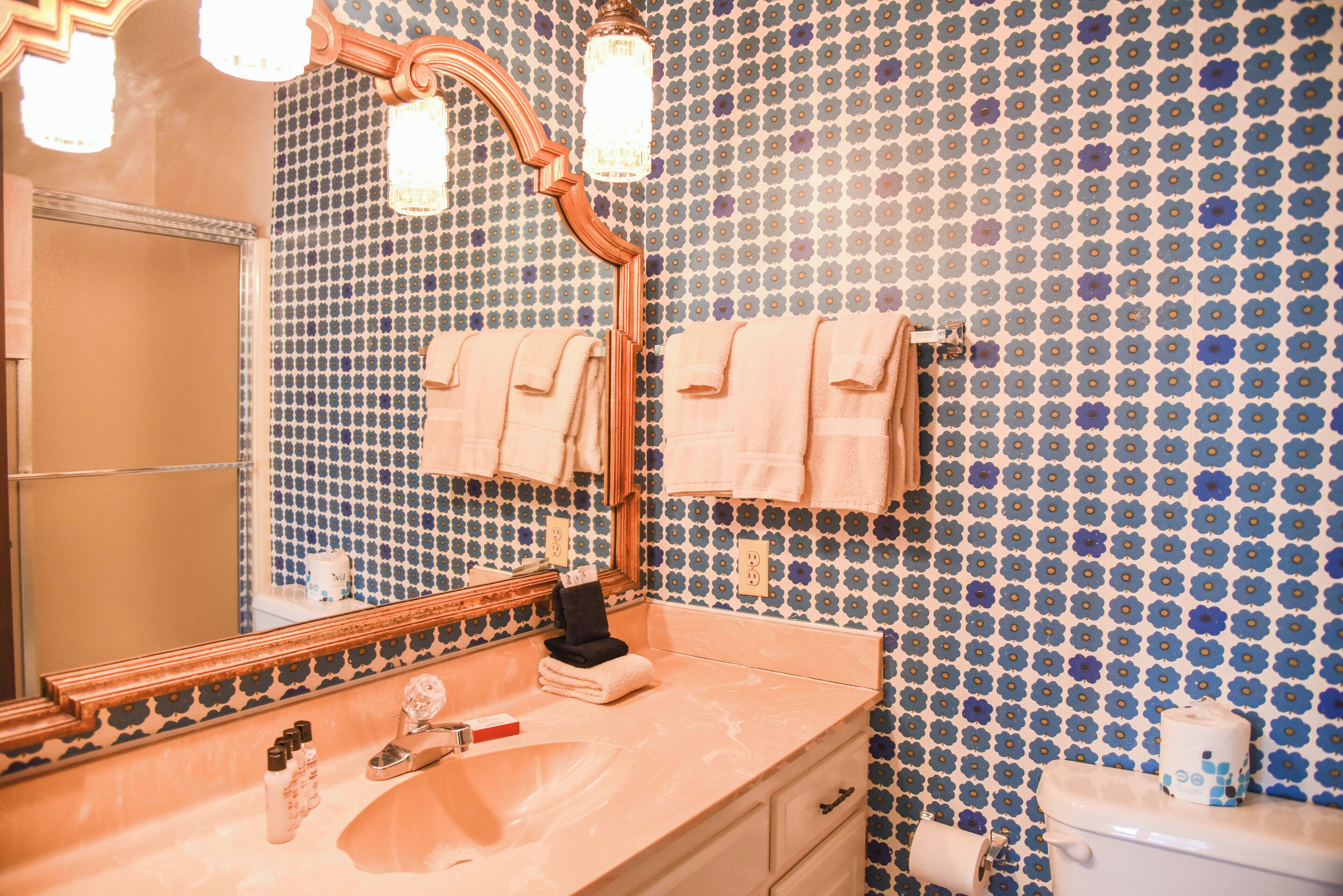 A bathroom with a mirror, sink, and toilet. The walls are tiled with a blue and white pattern.