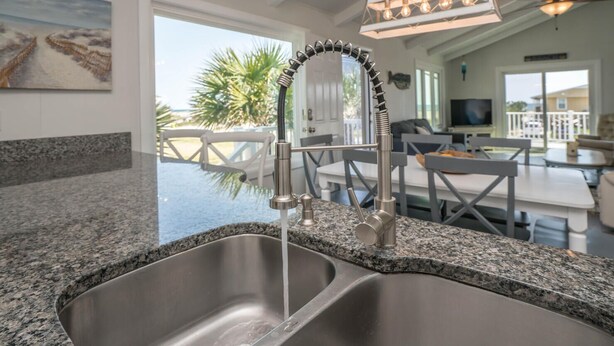 Una cocina con un lavamanos doble, grifo de acero inoxidable y encimera de granito. Se ve un comedor con asientos al aire libre a través de la ventana.
