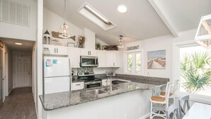 Una cocina moderna con armarios blancos, encimeras de granito y electrodomésticos de acero inoxidable.