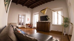 A living room with a leather sofa, a wooden coffee table, a TV on the wall, and a floor lamp.