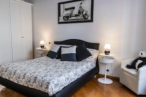 Quarto bem arrumado com cama, mesas de cabeceira, uma cadeira e luminária na parede.