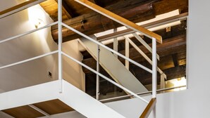 A multi-level wooden staircase with white railings and a green cushioned chair in a spacious room with wooden flooring and exposed beams.