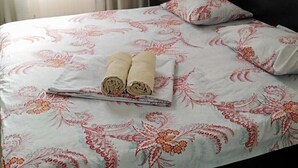 A neatly made bed with a floral bedspread, a rolled towel, and a pillow on a dark headboard in a room with a window and curtains. - Kedr Grad Inn on the way to Medeo (Almaty)