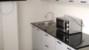 A compact kitchen with white cabinets, a stainless steel sink, a microwave, and a flat-screen TV mounted on the wall. - Kedr Grad Inn on the way to Medeo (Almaty)