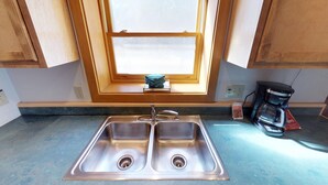 A kitchen with two stainless steel sinks, a window with a view, wooden cabinets, and a coffee maker on the counter. - 101 River Street Cabin (Red River)