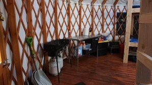 A tented accommodation with a wooden lattice wall, a table with various items, a bunk bed, and a door with a lock. - Snowshoe or ski and relax by a warm wood stove while playing games! (Scofield)