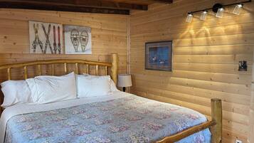 A wooden cabin bedroom with a bed, wooden headboard, wall-mounted light fixtures, and framed artwork.