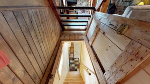 Un intérieur en bois avec un escalier menant à un niveau inférieur, une petite table en bois et un sol à carreaux.