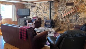 Un salon chaleureux avec un mur en pierre, une cheminée, des canapés en cuir, un téléviseur et un ventilateur de plafond.