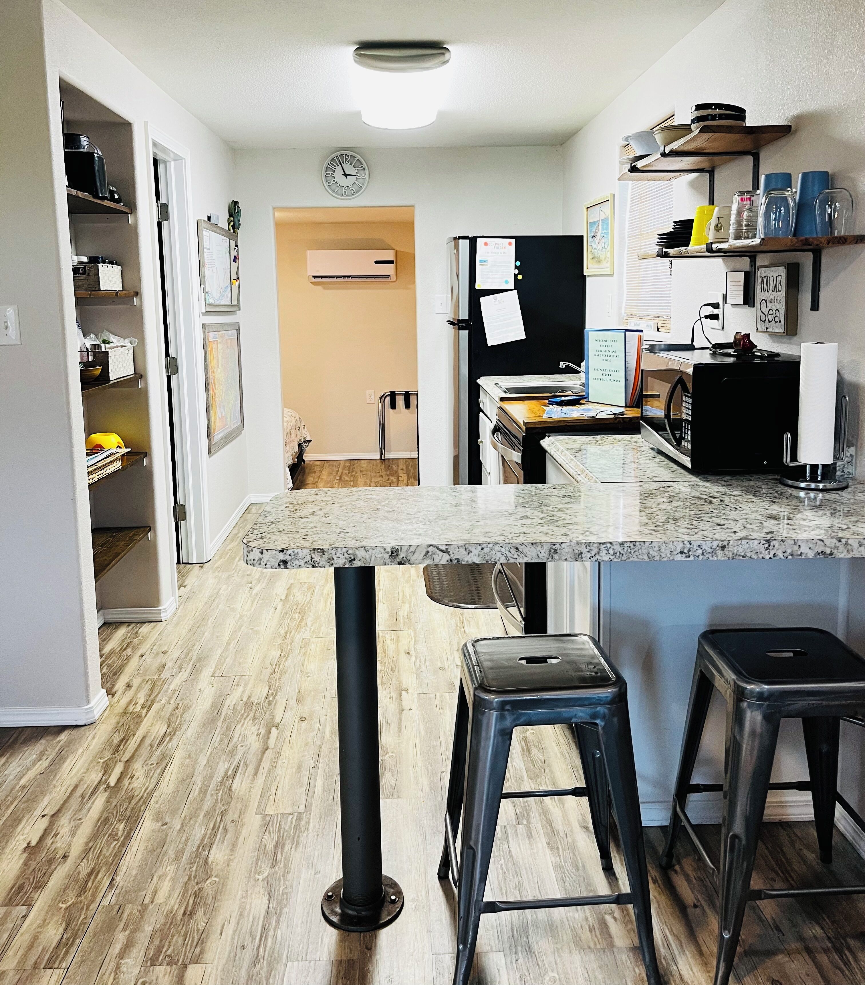 A kitchen with a marble countertop, wooden flooring, and a refrigerator.