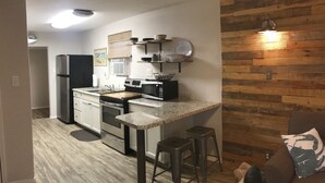 A modern kitchen with a central island, stainless steel appliances, and a wooden accent wall. - Vacay Getaway! Cozy Coastal South Bay Blue Bungalow (Rockport)