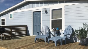A deck with Adirondack chairs, a small table, and a grill. - Vacay Getaway! Cozy Coastal South Bay Blue Bungalow (Rockport)