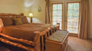 Een slaapkamer met een houten bedframe, een bankje aan het voeteneinde van het bed, een nachtkastje met een lamp en een raam met gordijnen.