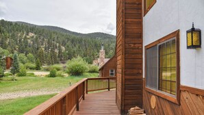 Een houten terras met een balustrade, een stenen schoorsteen en uitzicht op een bebost gebergte.