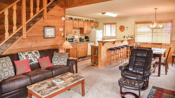 Een gezellig interieur van een chalet met een houten trap, een eethoek, een keuken en een woonkamer met een leren bank en een salontafel.