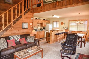 A cozy cabin interior with a wooden staircase, a dining area, a kitchen, and a living room with a leather sofa and a coffee table. - Our Red River Cabin on Tenderfoot (Red River)