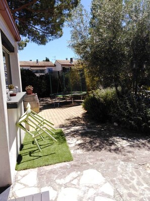 Un patio con un trampolín, un pequeño jardín y un sendero de piedra que lleva a una casa.