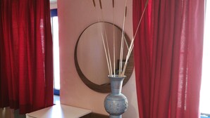 Une pièce avec un bureau blanc, un vase bleu orné d’éléments décoratifs et des rideaux rouges.