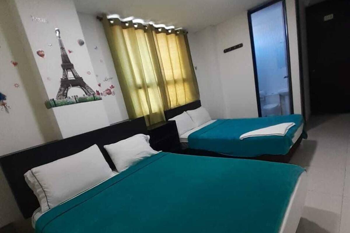 Habitación de hotel con dos camas, una ventana con cortinas, una puerta y una pared con una imagen de la Torre Eiffel.