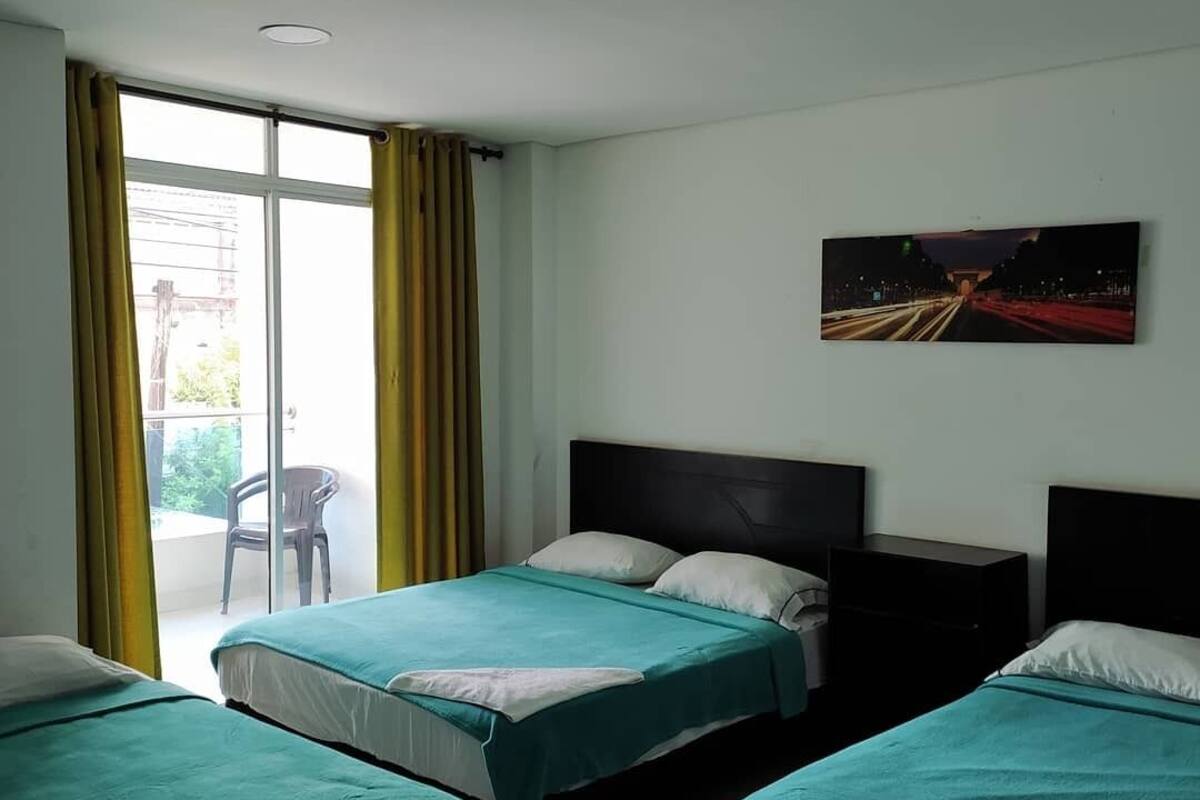 Una habitación de hotel con tres camas individuales, un ventanal con cortinas amarillas y un cuadro en la pared.