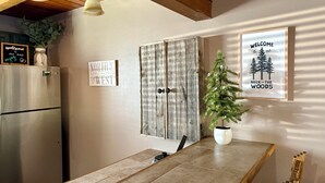 A kitchen with a wooden ceiling, a stainless steel refrigerator, a dining table with a potted plant, and two signs on the wall.