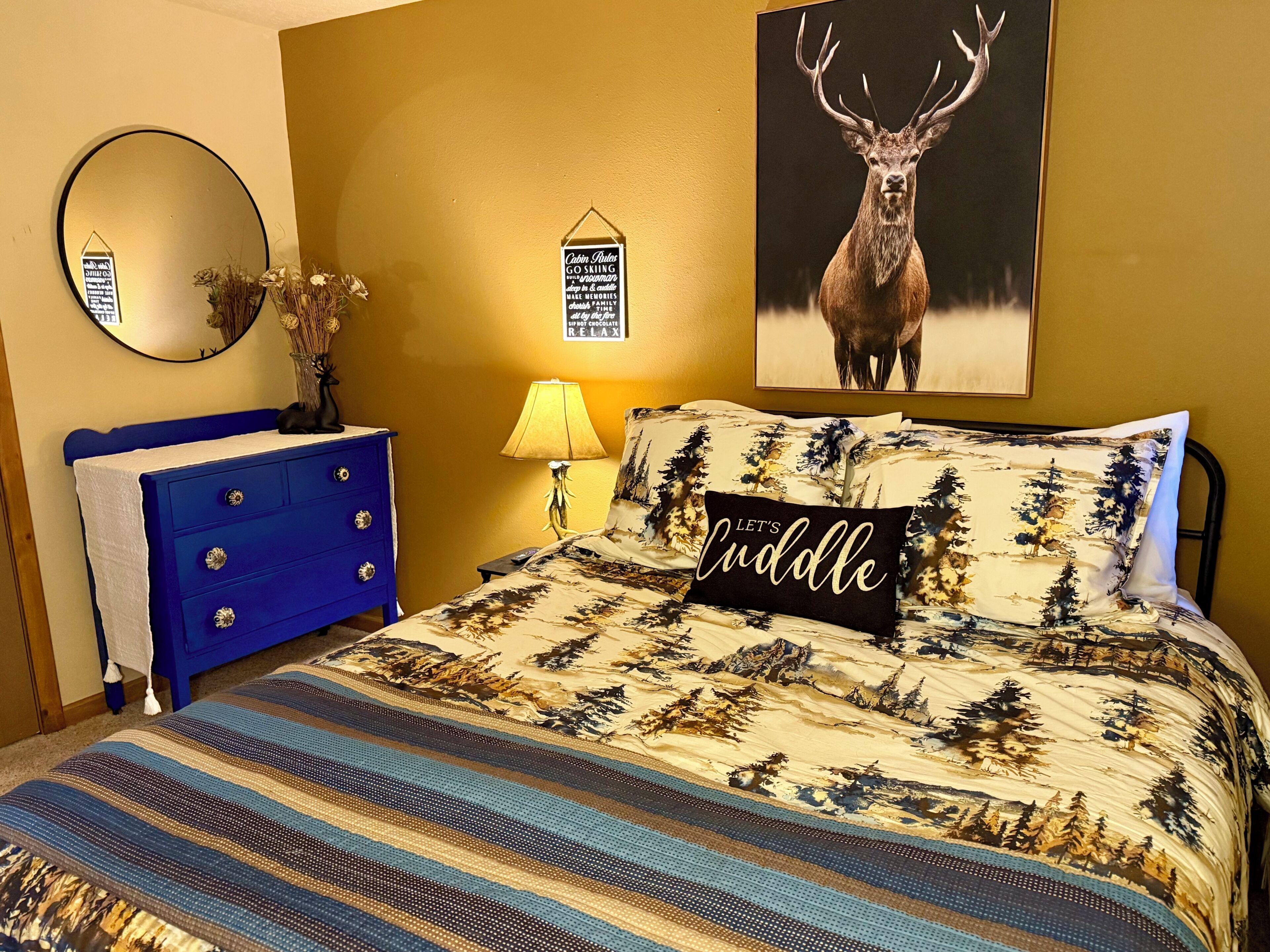 Ein Schlafzimmer mit einem Bett, einem Schminktisch, einem Spiegel, einer Lampe und einem Hirschposter.
