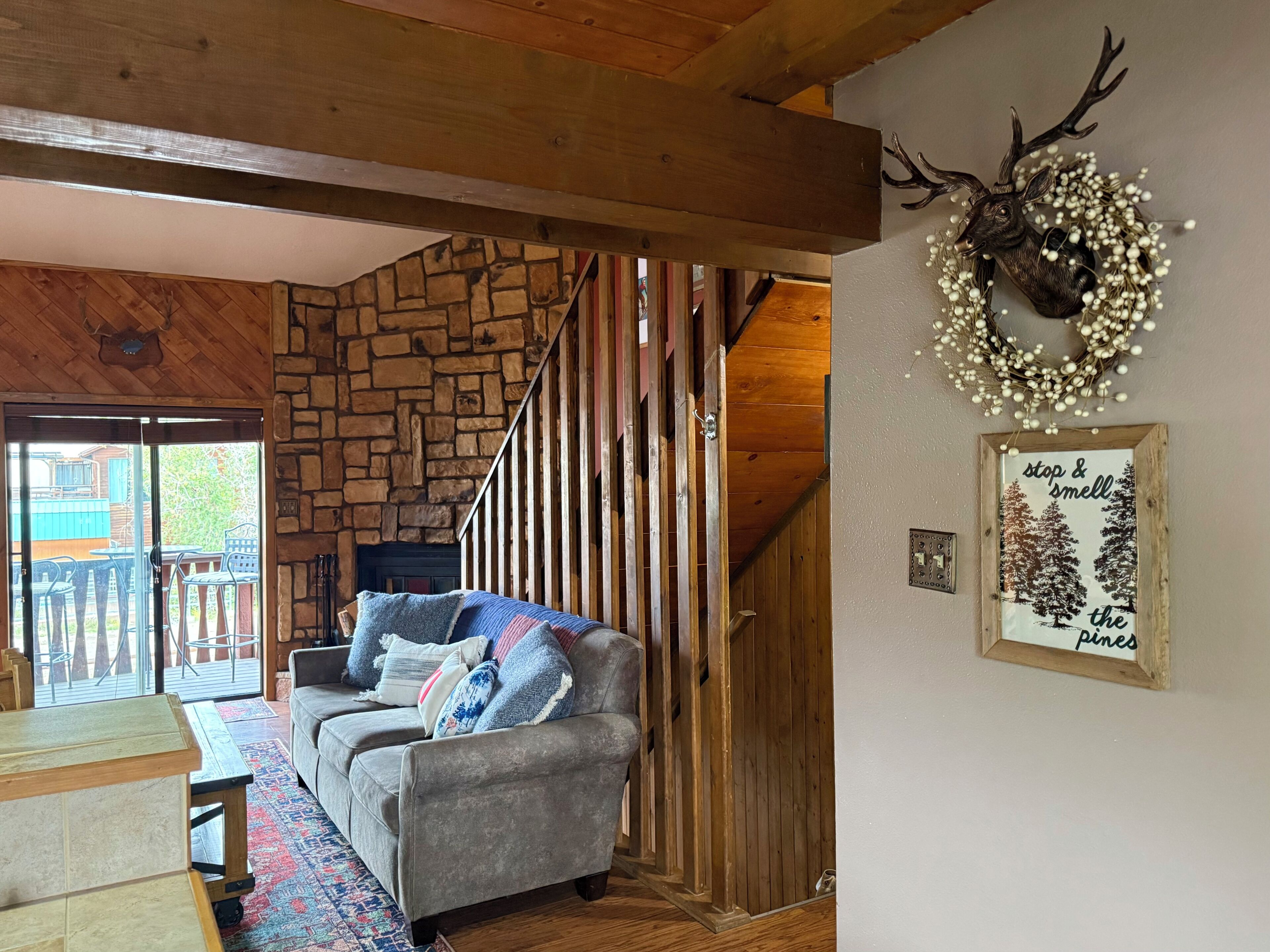 A cozy living room with a stone wall, a gray sofa, a wooden staircase, and a deer head decoration.